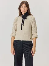 Buzo de lana color beige con mangas abullonadas de punto calado con diseño de rombos. Presenta cuello redondo y un aplique decorativo de flores negras con cinta de terciopelo en el cuello.