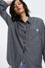 Camisa popelina rayada color rojo y blanco, con corte oversized, abotonadura frontal y en las mangas, y un bolsillo frontal.
