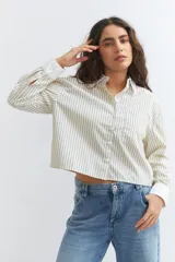 Camisa de manga larga con cuello y puños blancos contrastantes. El cuerpo de la camisa es de color crema con finas rayas verticales azules y tiene un corte crop.