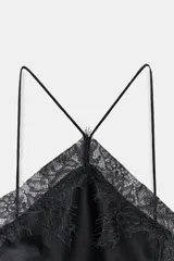 Vestido negro de satén con tirantes finos cruzados en la espalda y escote en V. Presenta aplicación de encaje en el escote y en el bajo asimétrico.