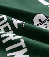 Remera de corte boxy y estilo deportivo, color verde oscuro, con diseño inspirado en el fútbol americano de Peanuts. Presenta cuello redondo, mangas cortas con franjas blancas horizontales y estampas localizadas de Snoopy en el frente.