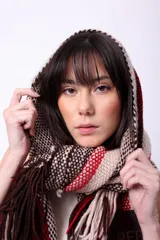 Bufanda de lana merino tejida en telar, con diseño de rayas en tonos marrón, beige y rojo. Presenta flecos en los extremos y un parche negro con la palabra "CAPER" en blanco.