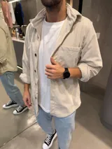 Sobrecamisa de pana color arena, con cuello camisero, cierre frontal de botones oscuros y un bolsillo en el pecho. Presenta un corte recto y mangas largas.