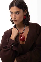 Collar corto con un gran medallón central de acrílico veteado en tonos rojos. La cadena está compuesta por una combinación de cuentas de acrílico, piedras naturales y cristales checos en colores rojo, azul, negro, gris y blanco.