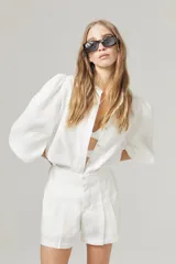 Short de lino blanco con cintura alta, tablas, bolsillos laterales y cierre frontal con gancho metálico.