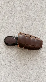 Zuecos de cuero marrón con diseño de tiras anchas entrelazadas estilo romano, punta cuadrada y plantilla plana negra con logo grabado de la marca.