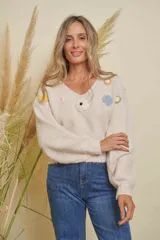 Buzo de punto color beige con cuello en V y mangas largas abullonadas. Decorado con apliques de flores tejidas en varios colores como amarillo, rosa, negro, azul y verde.