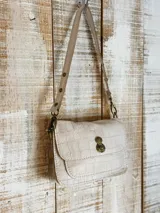 Minibag de cuero con textura de reptil, color beige, con solapa frontal y cierre metálico giratorio en tono bronce. Incluye una correa ajustable con detalles de tachas metálicas.