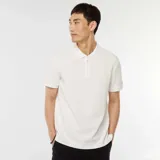 Remera polo blanca de piqué con cuello clásico, manga corta y cierre frontal con cremallera metálica.