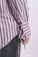 Camisa de manga larga con diseño de rayas verticales en tonos violeta y blanco, corte oversize, cuello camisero, cierre frontal con botones y detalles de lazos en el frente.