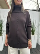 Polerón de punto color chocolate con cuello alto y diseño de trenza vertical en el centro. Presenta mangas largas con puños acanalados y un corte holgado.