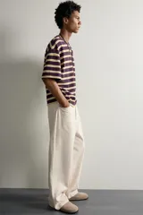 Camiseta de corte relaxed fit con diseño de rayas horizontales en tonos morado, amarillo y blanco. Presenta cuello redondo y mangas cortas.