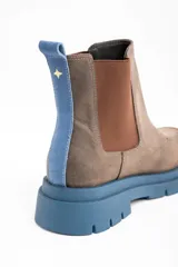 Bota tipo Chelsea de cuero lavado en tono marrón, con paneles laterales elásticos en color marrón oscuro. Presenta una suela track robusta de goma en color azul y un tirador trasero en el mismo tono azul.