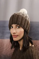 Gorro de punto degradé en tonos marrón y blanco, con diseño tejido en canalé y pompón superior claro.