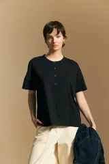 Remera de manga corta color negro, con cuello redondo y cierre frontal parcial con botones. Presenta un corte relajado y líneas simples.