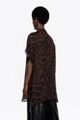 Camisa larga de corte recto, con diseño fluido, cuello camisero, botones frontales y mangas cortas tipo murciélago con vivo a lo largo de la costura. Presenta estampado animal print en tonos marrón y negro.