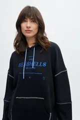 Canguro color crudo con capucha, cordón de ajuste celeste, bolsillo tipo canguro, puños y ruedo acanalados, y estampado frontal con la frase "The Seashells".