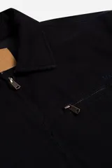 Campera de canvas con diseño utilitario, color negro, con cierre frontal y bolsillo con cierre en el pecho. Presenta cuello camisero y detalles metálicos en los tiradores de los cierres.