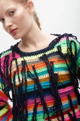 Buzo tejido al crochet con diseño a rayas horizontales multicolores y flecos colgantes.