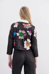 Saco corto de lentejuelas negras con bordados florales multicolores hechos a mano. Presenta cuello redondo, mangas largas y cierre frontal con ganchos invisibles.