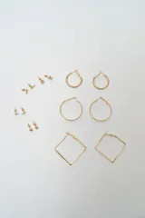 Set de siete pares de aros dorados de diversos diseños, incluyendo aros tipo argolla redondos en dos tamaños, aros cuadrados con textura y varios modelos de aros pequeños tipo broquel con detalles de piedras y esferas.
