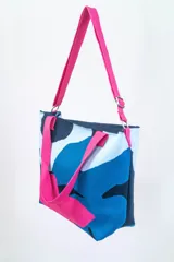 Bolso tipo tote con estampado abstracto en tonos azul, blanco, negro y verde. Tiene doble asa de mano y correa larga regulable al hombro, ambas en color negro.