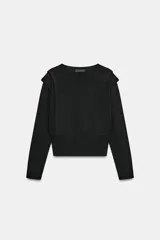 Jersey negro de punto, manga larga, con cuello redondo y detalle de pliegues o volados en la zona de los hombros.