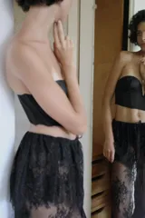 Falda midi semitransparente de tiro medio, confeccionada en tejido de encaje negro con detalle de superposición en la cintura y ajuste con lazada. Presenta bajo acabado en ondas y abertura en la espalda.