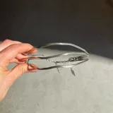 Gargantilla rígida de diseño triple con estructura ondulada en metal dorado, que se completa con una cadena fina ajustable en la parte posterior.