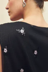 Top negro sin mangas de tul bordado con pequeñas lentejuelas en forma de flores y escote cruzado.