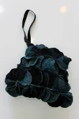 Cartera de mano verde oscuro hecha de círculos de lana merino afieltrada teñida artesanalmente, con asa de cuero marrón.