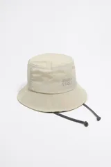 Gorro tipo bucket color beige, de nylon, con interior a rayas y cordón ajustable. Presenta logo bordado de la marca Bimba y Lola en el frente.
