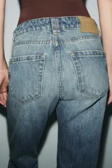 Jeans de tiro medio con corte slim leg, confeccionados en denim color beige. Presentan cintura con trabillas, diseño clásico de cinco bolsillos y cierre frontal con cremallera y botón metálico.