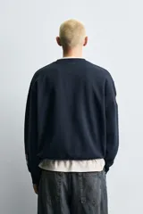 Sudadera de cuello redondo y manga larga en color azul marino, con corte relajado. Presenta múltiples parches decorativos y estampados a contraste en el frente y las mangas, con terminaciones en rib.