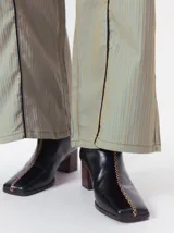 Botas de cuero color marrón con caña media y punta cuadrada. Presentan un cierre trasero, tirador para calzar fácilmente y bordado en color contrastante en el empeine. Suela de goma y taco de madera de 6 cm de altura.