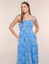 Vestido midi color azul con bordado broderie floral en tono blanco, escote recto con tirantes finos de lazo para anudar, corte ajustado en la cintura y falda escalonada holgada con bolsillos laterales.