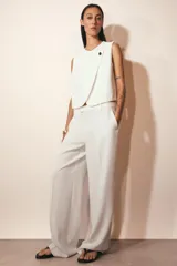 Chaleco blanco de cuello redondo y sin mangas, con cierre frontal cruzado con un botón.