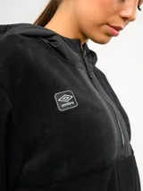 Buzo de polar negro con capucha, cierre frontal parcial y bolsillos laterales. Presenta detalles en nylon a tono en la capucha, la solapa del cierre y los bordes de los bolsillos, con el logo de la marca bordado en el pecho.