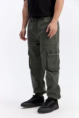 Pantalón cargo color tostado de corte amplio, con cintura elástica y cordón ajustable. Cuenta con bolsillos laterales con tapa en las piernas y puños elastizados en los tobillos.