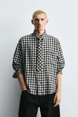 Camisa de corte relajado confeccionada en tejido fluido con estampado de cuadros. Presenta cuello solapa, cierre frontal de botones, manga larga con puños abotonados y una corbata integrada del mismo tejido.