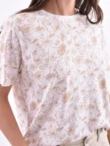 Remera de manga corta color beige con estampado de bananas en tonos amarillo, naranja y rosado.