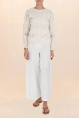 Suéter de punto calado color beige, de corte holgado y caída natural. Presenta un cuello redondo y mangas largas, ligeramente abullonadas, con detalles de calado y bordes festoneados.