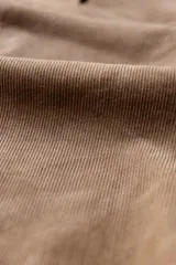 Camisa de manga larga confeccionada en pana gruesa color beige, con cuello abotonado, cierre frontal con botones y un bolsillo en el pecho con etiqueta decorativa.
