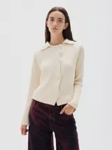 Cardigan de punto acanalado color crema, con cuello polo, cierre frontal de botones tejidos y manga larga.