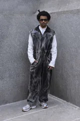 Mono de jean con lavado gris efecto desgastado, con múltiples cortes estructurales, cierre frontal oculto por cartera, cintura elástica y bordado de logo en azul. Incluye un pequeño accesorio de bolso desmontable para la cintura.