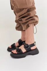 Sandalias de plataforma con suela de goma negra y tiras de cuero sintético color beige con cierre de velcro ajustable.