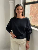 Sweater negro de punto con diseño de mangas tipo murciélago, cuello redondo y puños ajustados. Presenta un sutil patrón de líneas verticales en el tejido.
