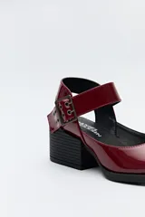 Zapato negro tipo zueco con acabado charol, tira ancha con hebilla metálica y taco ancho de altura media.