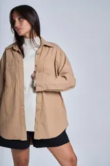 Sobrecamisa color beige confeccionada en gabardina, de corte holgado, con cuello camisero, cierre frontal con botones, dos bolsillos de parche en el pecho y mangas largas con puños abotonados.