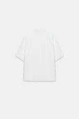 Camisa de manga corta y corte fluido, color marrón, con cuello solapa y cierre frontal con botones ocultos. Presenta bajo asimétrico con aberturas laterales y mangas con vuelta.
